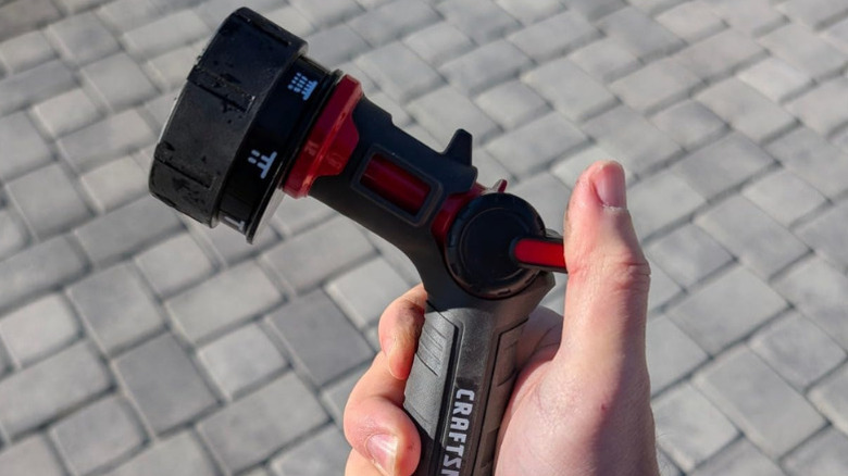 A hand holding Craftsman's Heavy-Duty 7-Pattern Water Nozzle over a paver patio