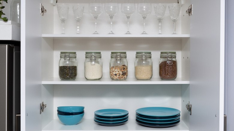 Various seeds in storage jars in pantry, white modern kitchen in background.