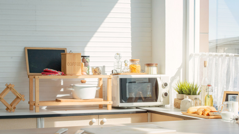 Sun coming in a kitchen window and landing on walls and counter with microwave.