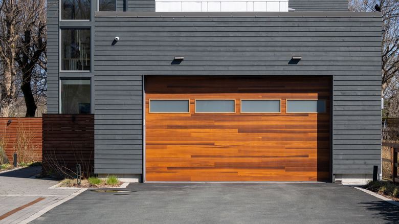 A modern brown wooden exterior garage door with four small horizontal glass windows.