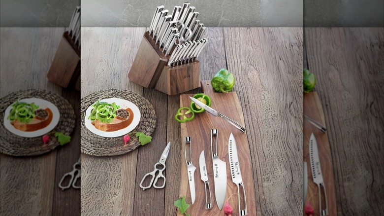 Knives in a knife block with four knifes on a cutting board, one knife resting on a fresh cut pepper on the cutting board, and shears to the right of the cutting board next to a plate of food