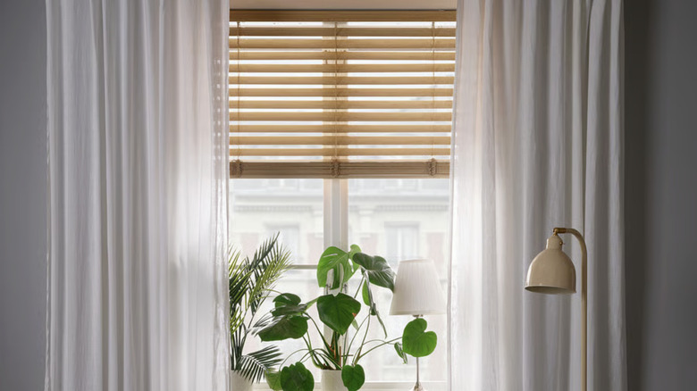 IKEA's VECKLARFLY Venetian blind in bamboo paired with white curtains in a living room