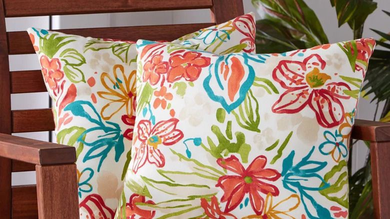 Two colorful Floral Square Outdoor Throw Pillows from Kensington Gardens on a wooden patio chair