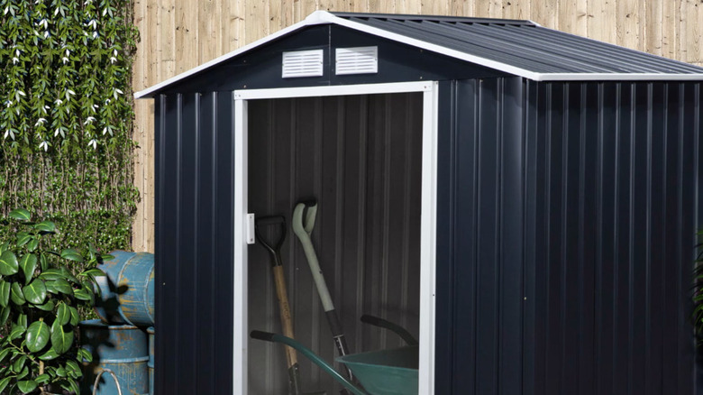 Outsunny's Metal Storage Shed with garden equipment inside, next to a fence.