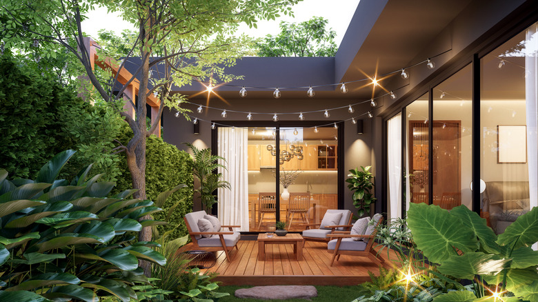 A raised patio with furniture, decorated with string lights and adjoined to a house with large glass doors.