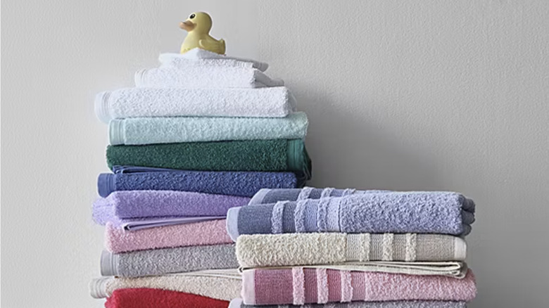 Gray and white towels are folded neatly on a cart with a travel makeup back hanging off of it.