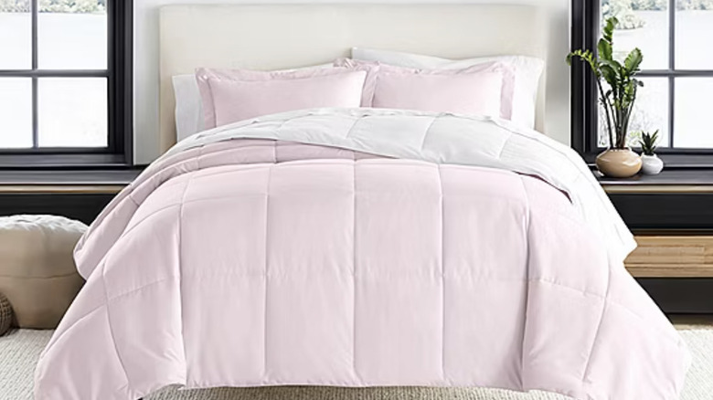 A pink comforter and pillows are on a bed next to a table with a lamp.