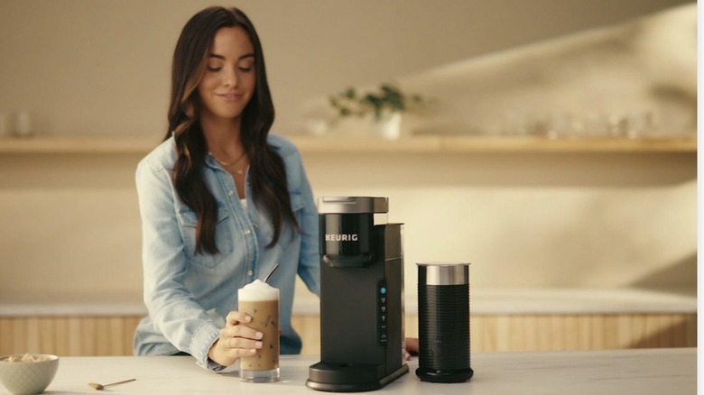A woman makes an iced coffee drink with a Keurig machine.