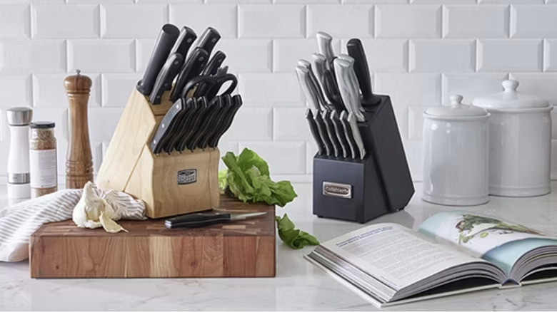 Two knife sets sit on a countertop with a cookbook and jars.