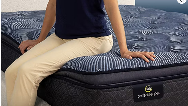 A person in khaki pants and a blue shirt sits on top of a Serta mattress.