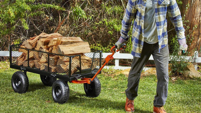 A person pulling a garden cart loaded with chopped logs