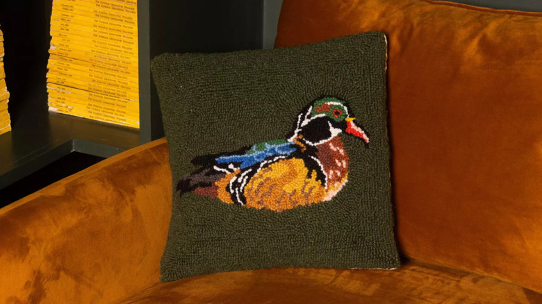 The Wood Duck Green Throw Pillow from Makers Collective on a brown upholstered sofa
