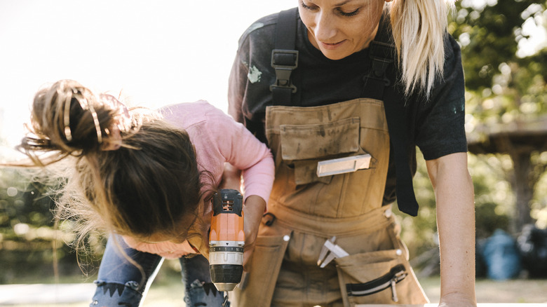Woman teaching daughter to use a drill