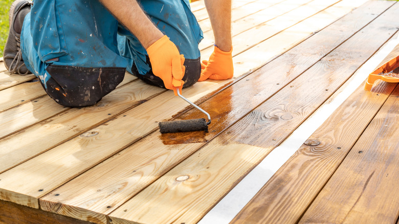 Person applying stain to a deck with a brush.