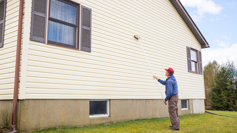 Man uses long handled scrub brush to clean vinyl siding on his house