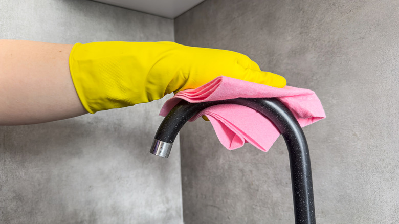 Yellow gloved hand wiping a clean faucet dry with a pink cloth
