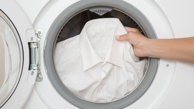 Hand loading a white shirt into a washing machine