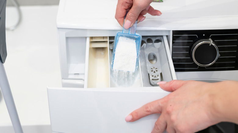 A hand adding detergent to a washing machine drawer