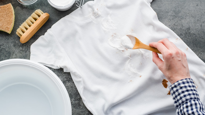 A person's hand sprinkling baking soda over a white t-shirt
