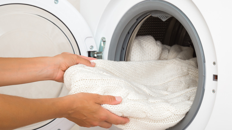 A person's hands loading whites into a washing machine