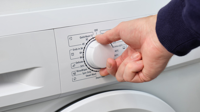 A hand adjusting the settings dial on a washing machine