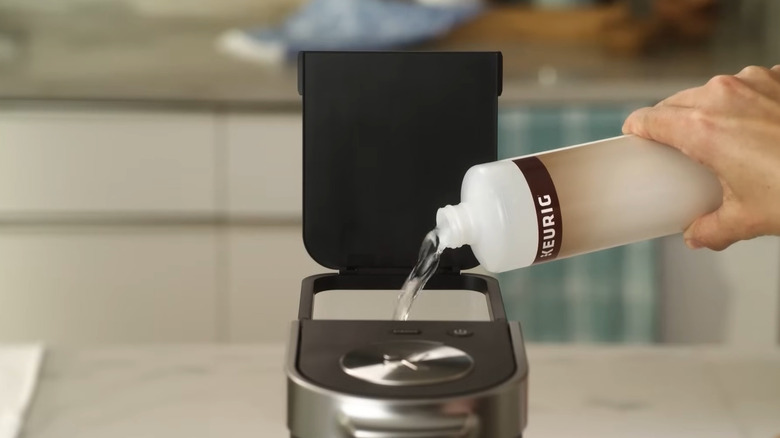Person pouring Keurig descaling solution into a Keurig coffee machine