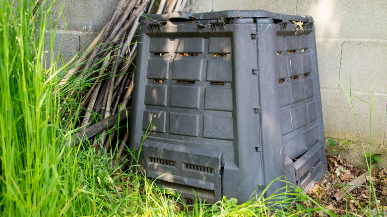 Black composting bin in the corner of a yard