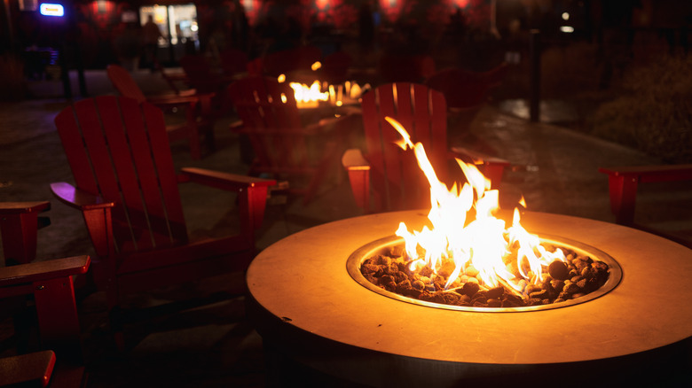 Outdoor gas fire pit surrounded by red Adirondack chairs