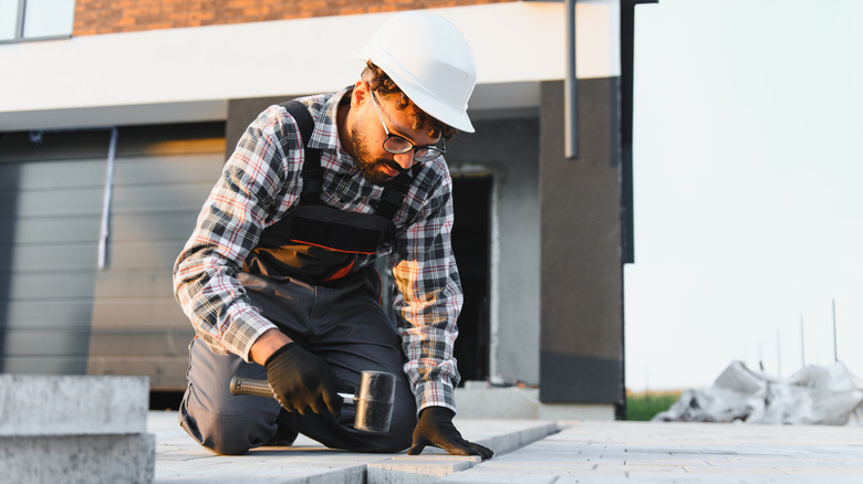 A person in a hard hat installing pavers on a driveway