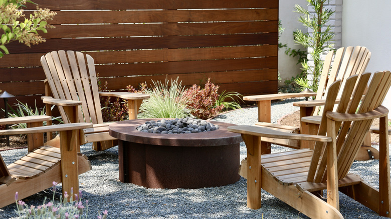 A backyard fire pit surrounded by gravel and deck chairs
