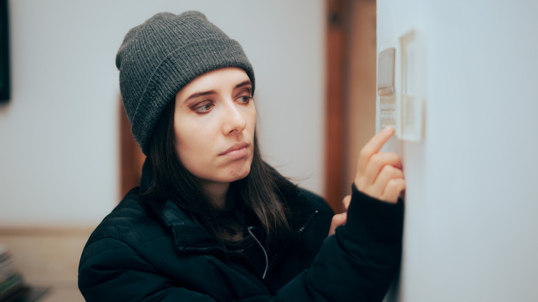 Woman wearing jacket and hat adjusting home thermostat