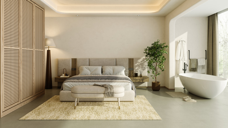 Minimalist bedroom with ottoman at the foot of the bed, white freestanding tub to the right of the bedroom.