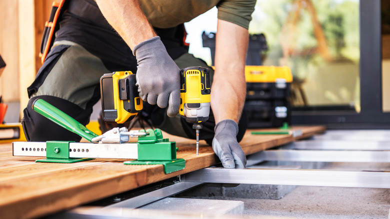 A contractor working on adding wooden flooring over a metal frame outside to make a deck