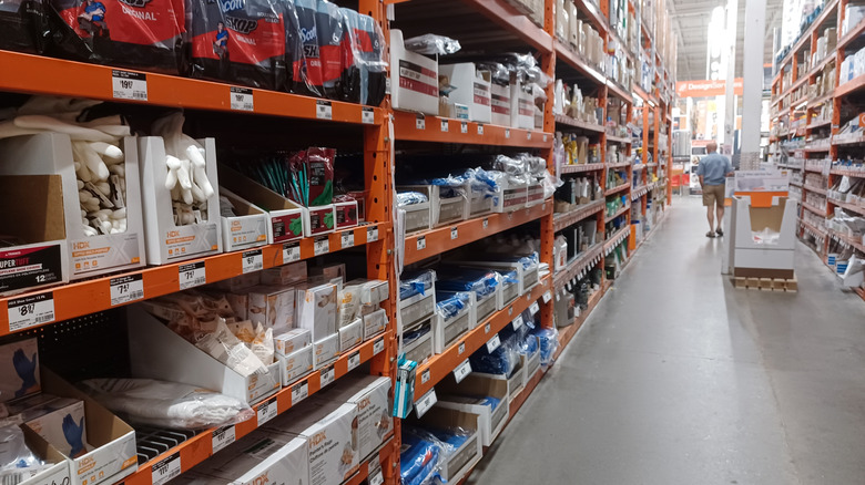An isle in Home Depot filled with products and with a person walking away from the camera