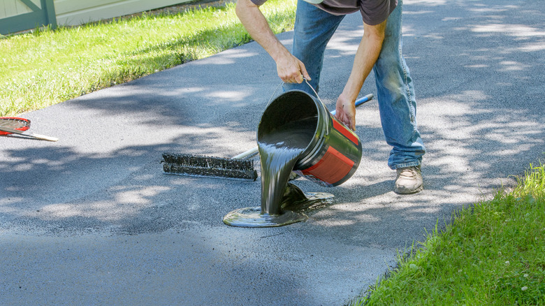 Homeowner pouring asphalt sealant onto driveway