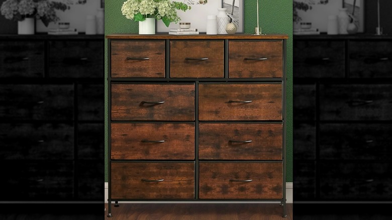 The brown Bigleap 9 Drawer Dresser against a green wall with white decor items on top.