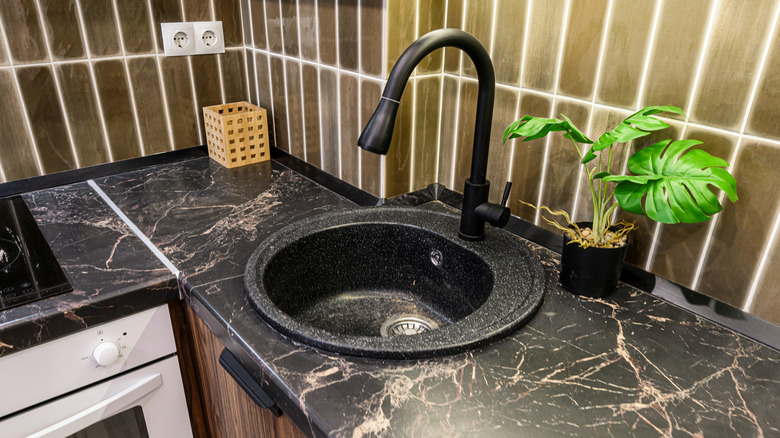 Black kitchen sink on black marble countertop with brown cabinet and backsplash