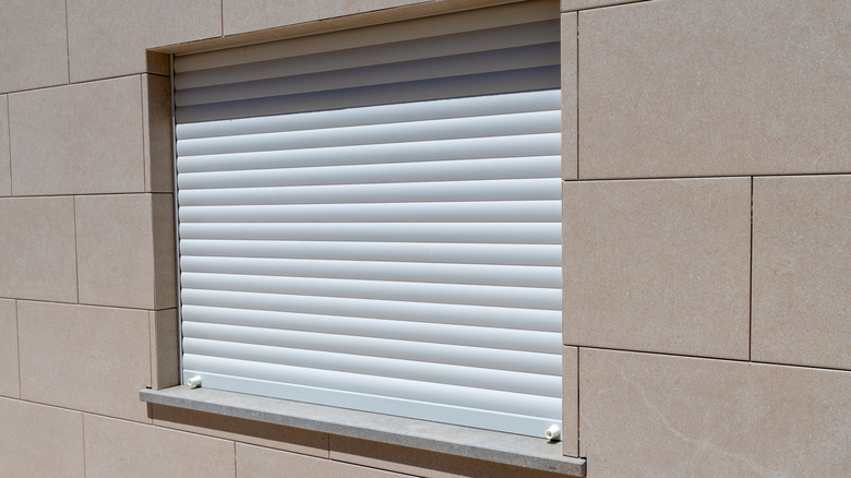 stone block wall with window covered by white rolling shutter