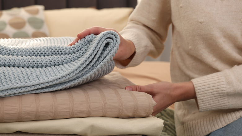 A hand reaching towards folded blankets.