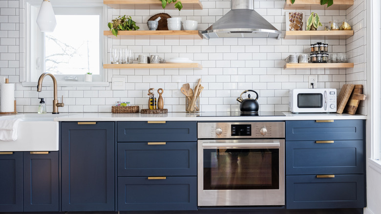 A kitchen with dark blue cabinets, timber shelving and white benchtops