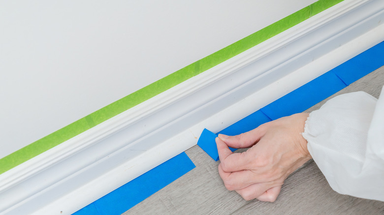 Hand applying blue painter's tape below a strip of green painter's tape