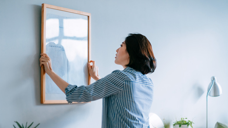 woman hanging art on wall