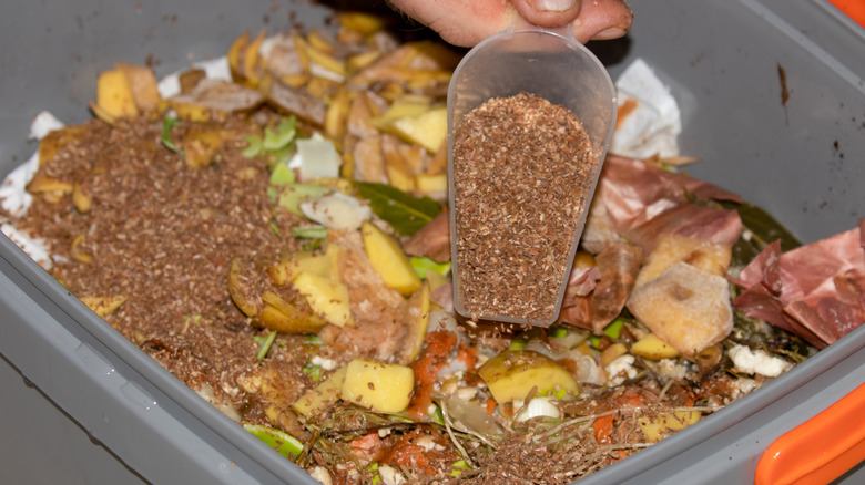 A scoopful of bokashi bran being added to a bucket of compost.