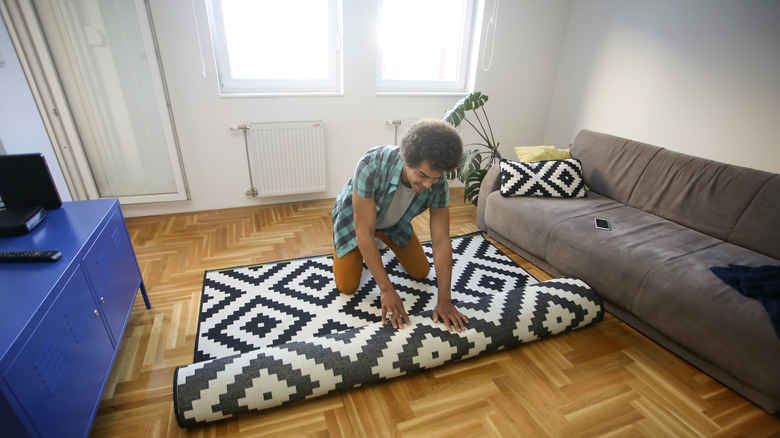 Man rolling out a black and white monochrome area rug in his living room.