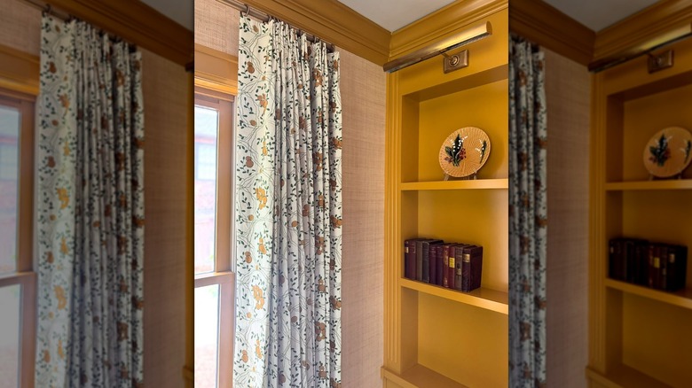 Pink textured wall with mustard yellow trim and built-in bookcase and floral curtain