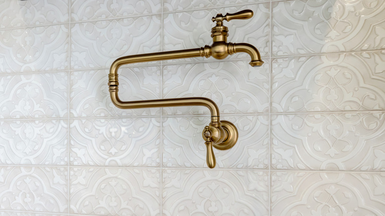 A brass pot filler mounted to vintage tiles.