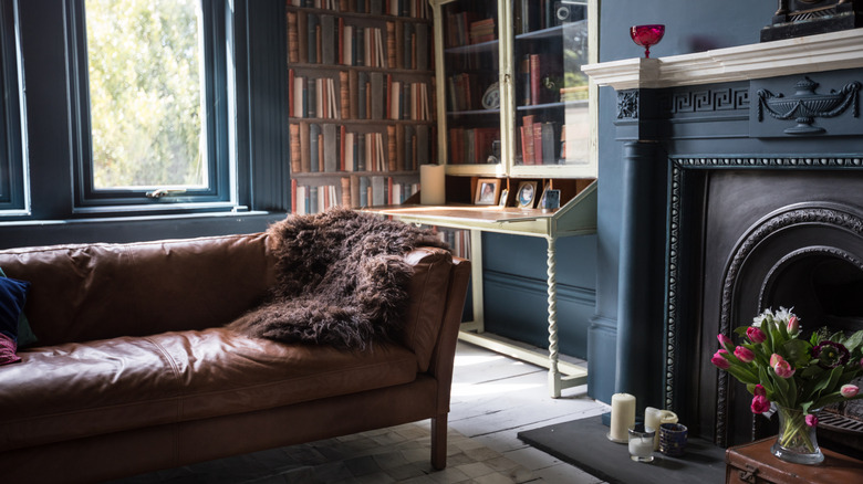 A dark and moody living room interior with brown leather sofa and painted navy blue walls and mantel