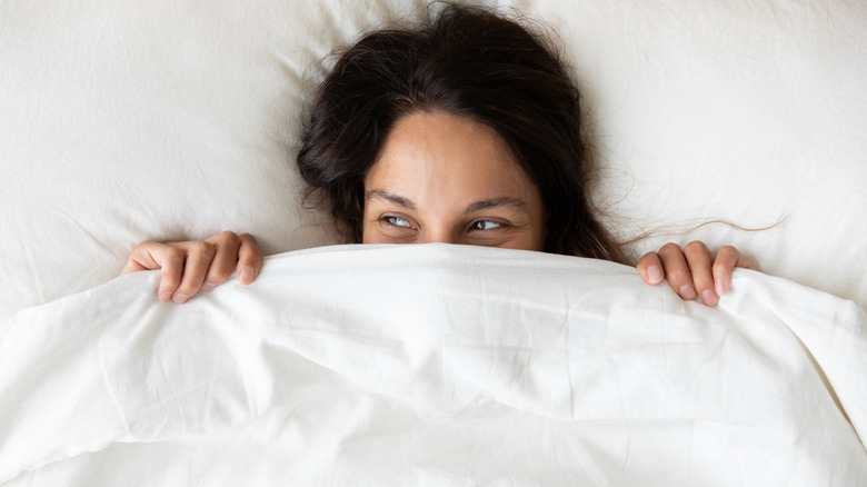 A woman lying on her bed with a sheet pulled up to her face