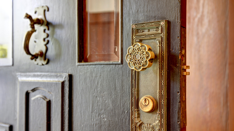 A close up of an elaborate brass door handle on the front of an antique door.