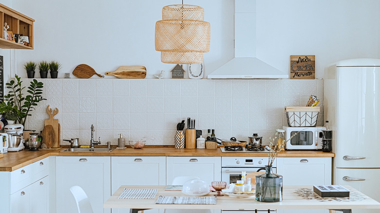 A modern white kitchen has depth due to warm wood, an eye-catching light fixture and accessories